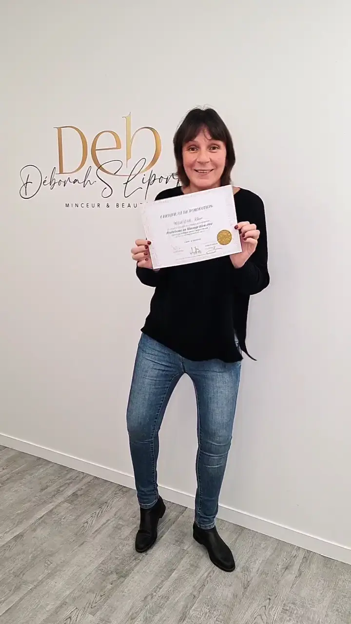 Stagiaire tenant son certificat de formation devant le mur au lettrage doré du centre.