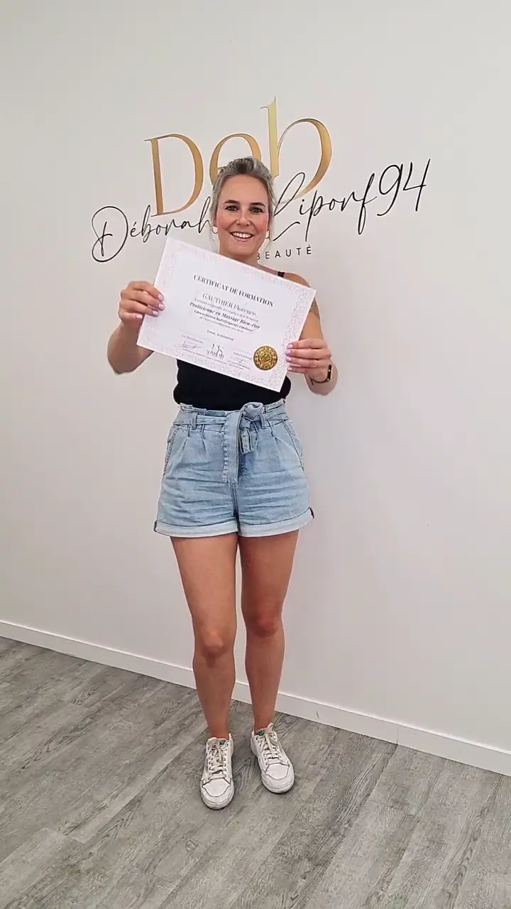 Stagiaire tenant son certificat de formation devant le mur au lettrage doré du centre.