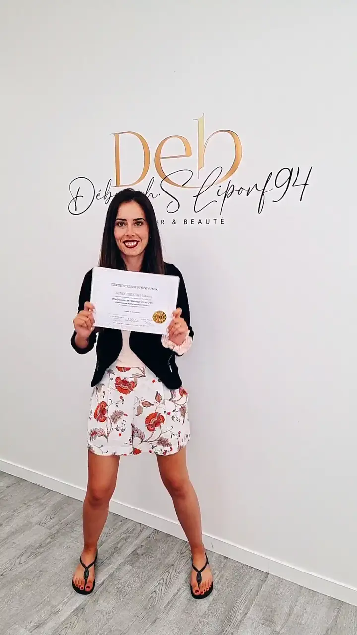 Stagiaire tenant son certificat de formation devant le mur au lettrage doré du centre.
